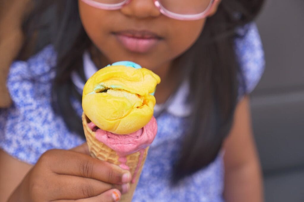 A child enjoys a vibrant multi-colored ice cream cone on a sunny day.
