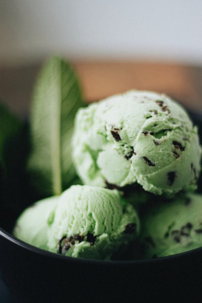 Close-up of artisanal mint chocolate chip ice cream with fresh mint leaves in a bowl.